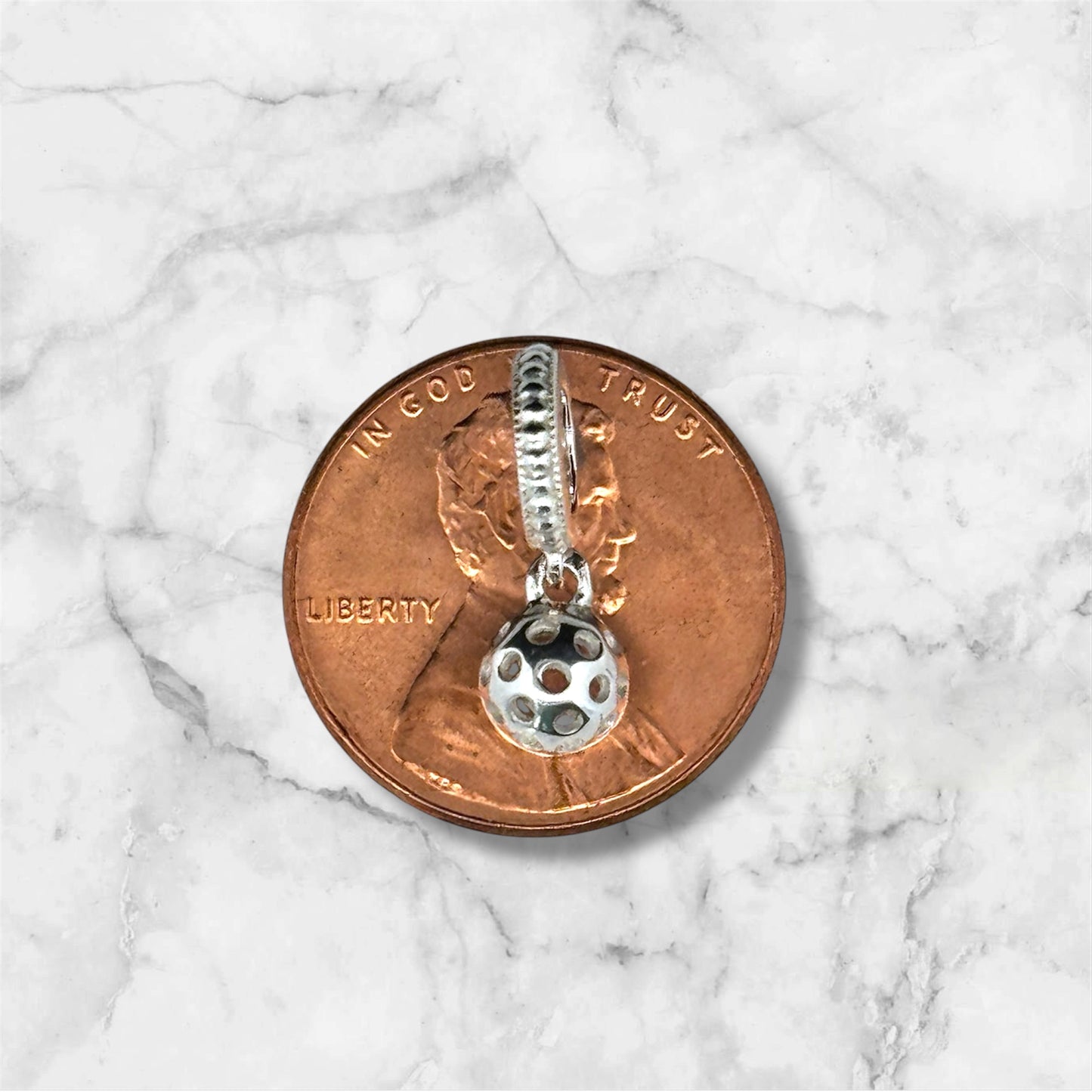 pickleball ball charm laying on copper penny, sterling silver