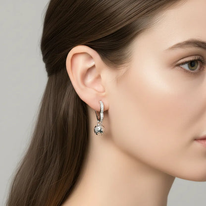 Close-up of a woman wearing a silver heart huggie earring with a pickleball dangle.