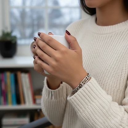 Person holding a white mug showcasing a pickleball court bracelet on her wrist, background indoor scene is blurred 