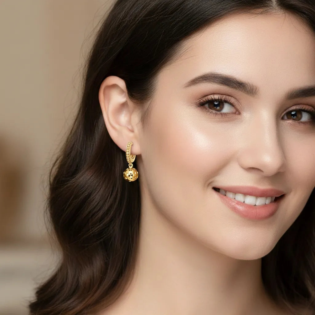 Close-up of a woman wearing gold pickleball huggie earrings with a blurred background