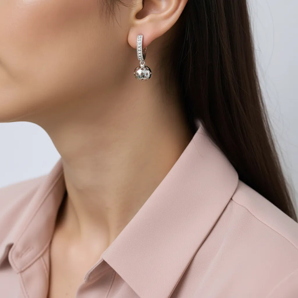 Close-up of a person wearing a silver huggie earring  with pickleball dangle