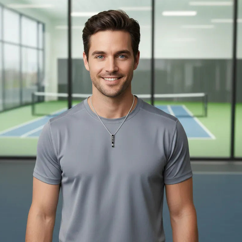 Man standing on a pickleball court wearing a gray t-shirt and silver necklace
