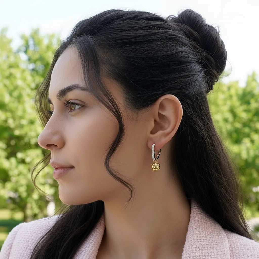 Woman with styled hair and earrings, outdoors with greenery in the background.