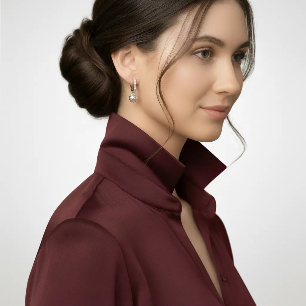 Woman wearing a burgundy shirt and silver earring with a plain background