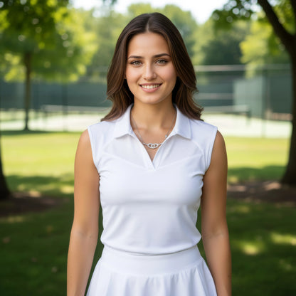 Woman in a white sleeveless dress standing outdoors with greenery in the background. Woman is wearing a silver necklace with double pickleball paddle pendant and ball charm.
