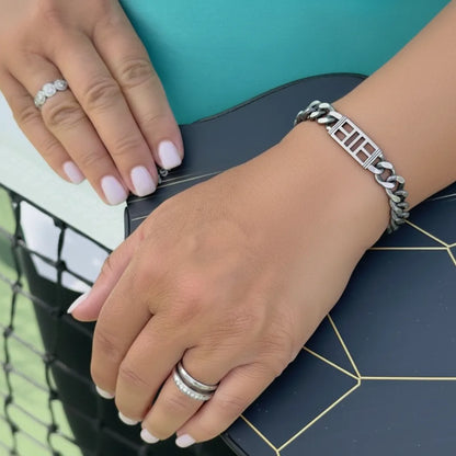 Close-up of woman's hands resting on a pickleball paddle with a pickleball court bracelet on her wrist