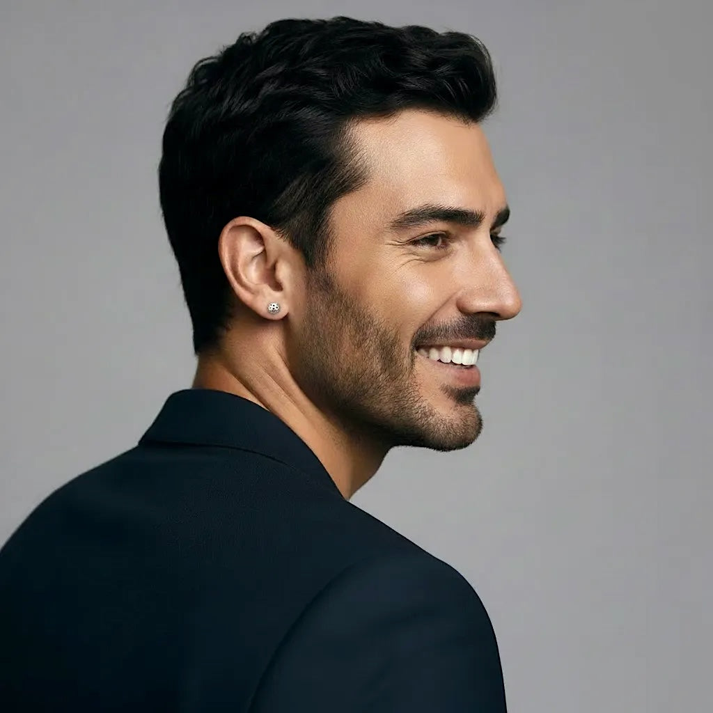 Man with a stylish haircut and beard, wearing a dark suit and silver pickleball stud earrings, against a gray background
