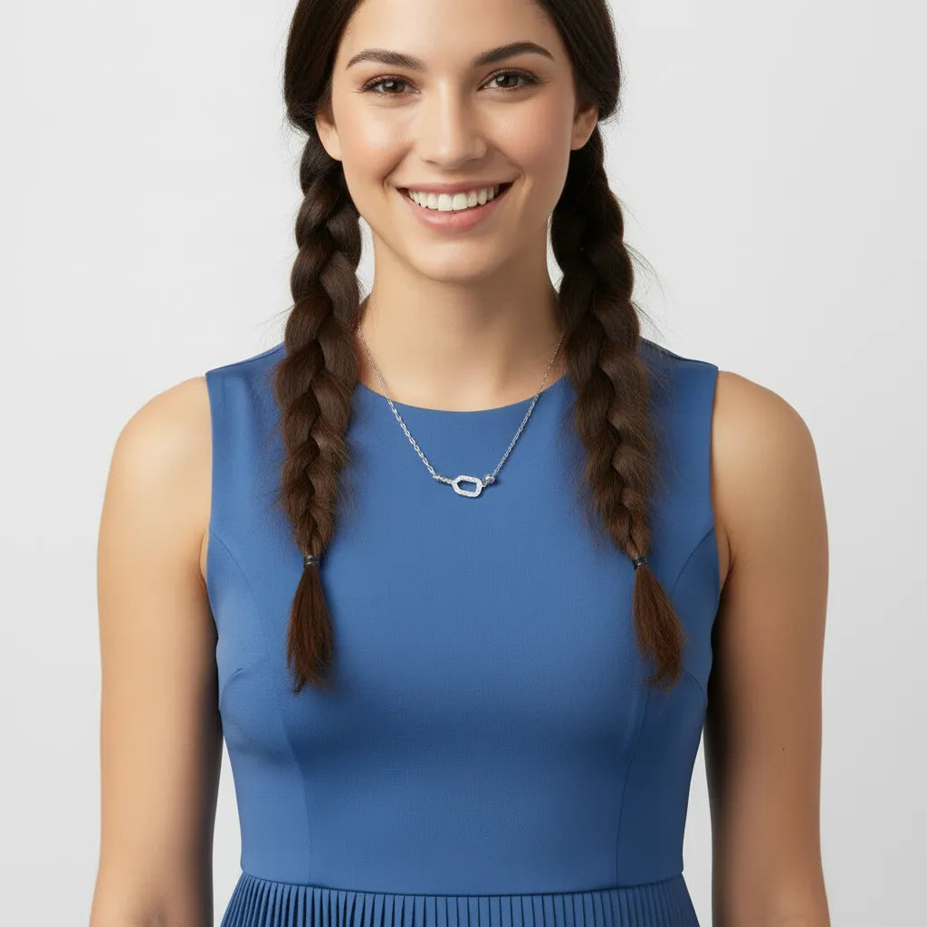 Woman wearing a silver necklace and a blue sleeveless top with braided hair against a light gray background