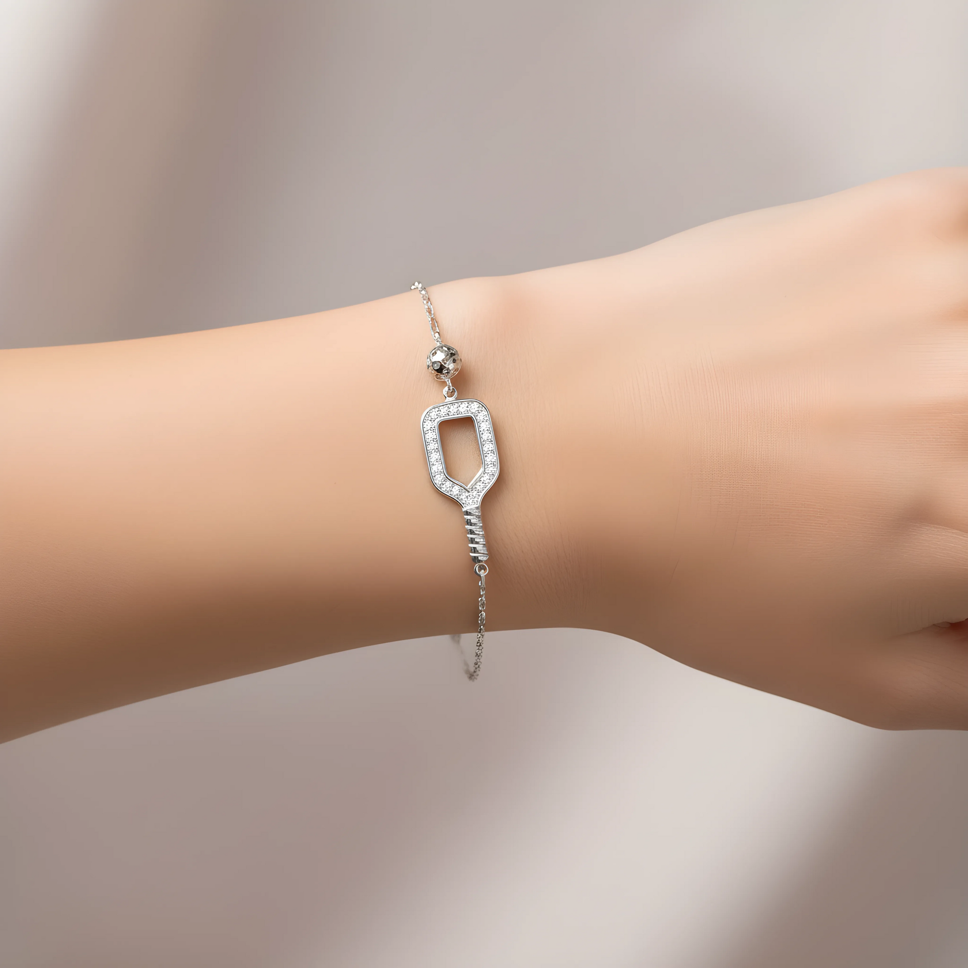 Silver pickleball paddle and ball bracelet worn on a wrist against a neutral background.