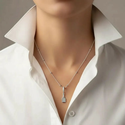 Silver pickleball necklace with a paddle charm pendant on a woman wearing a white shirt.