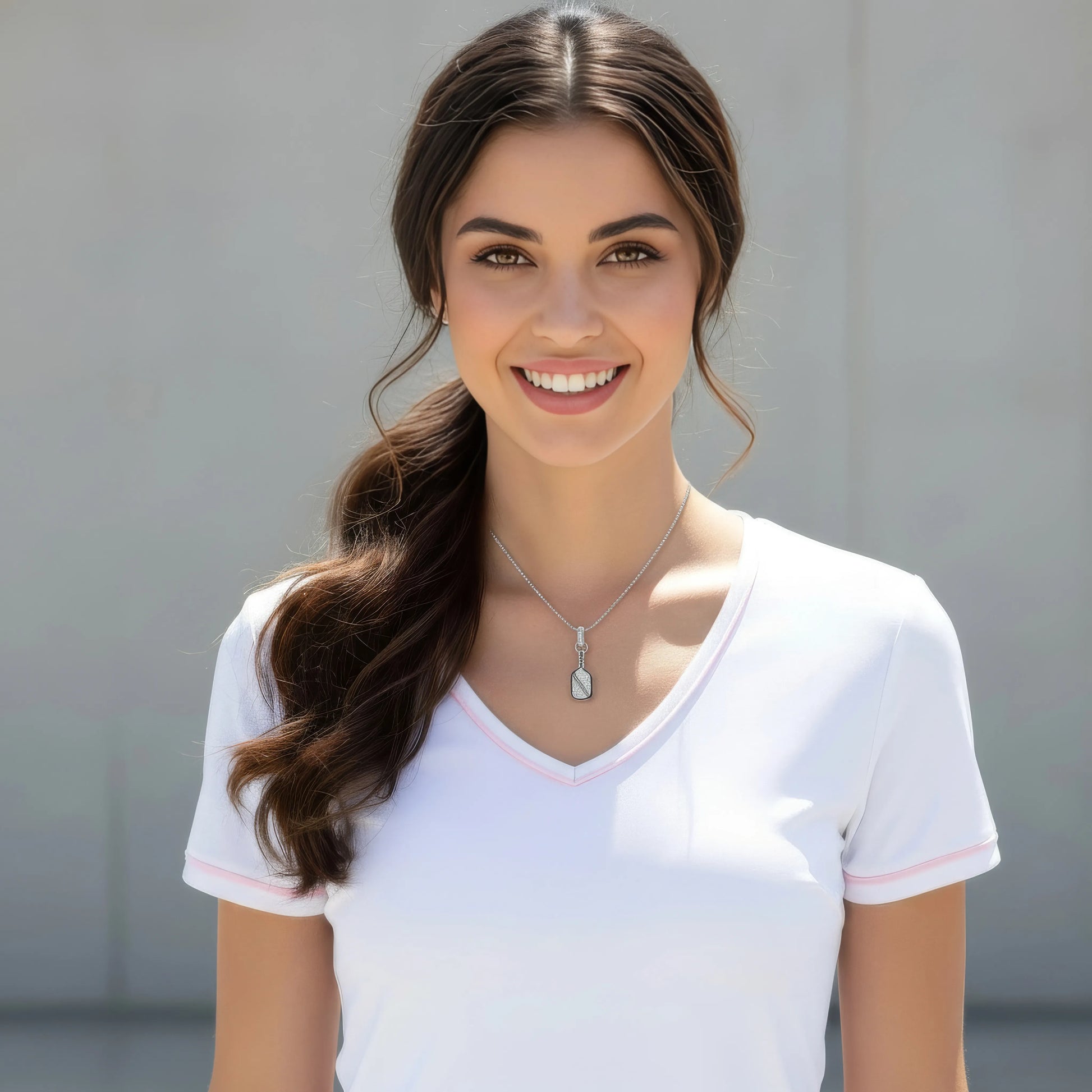Woman wearing a white shirt and a pickleball paddle necklace with a neutral background