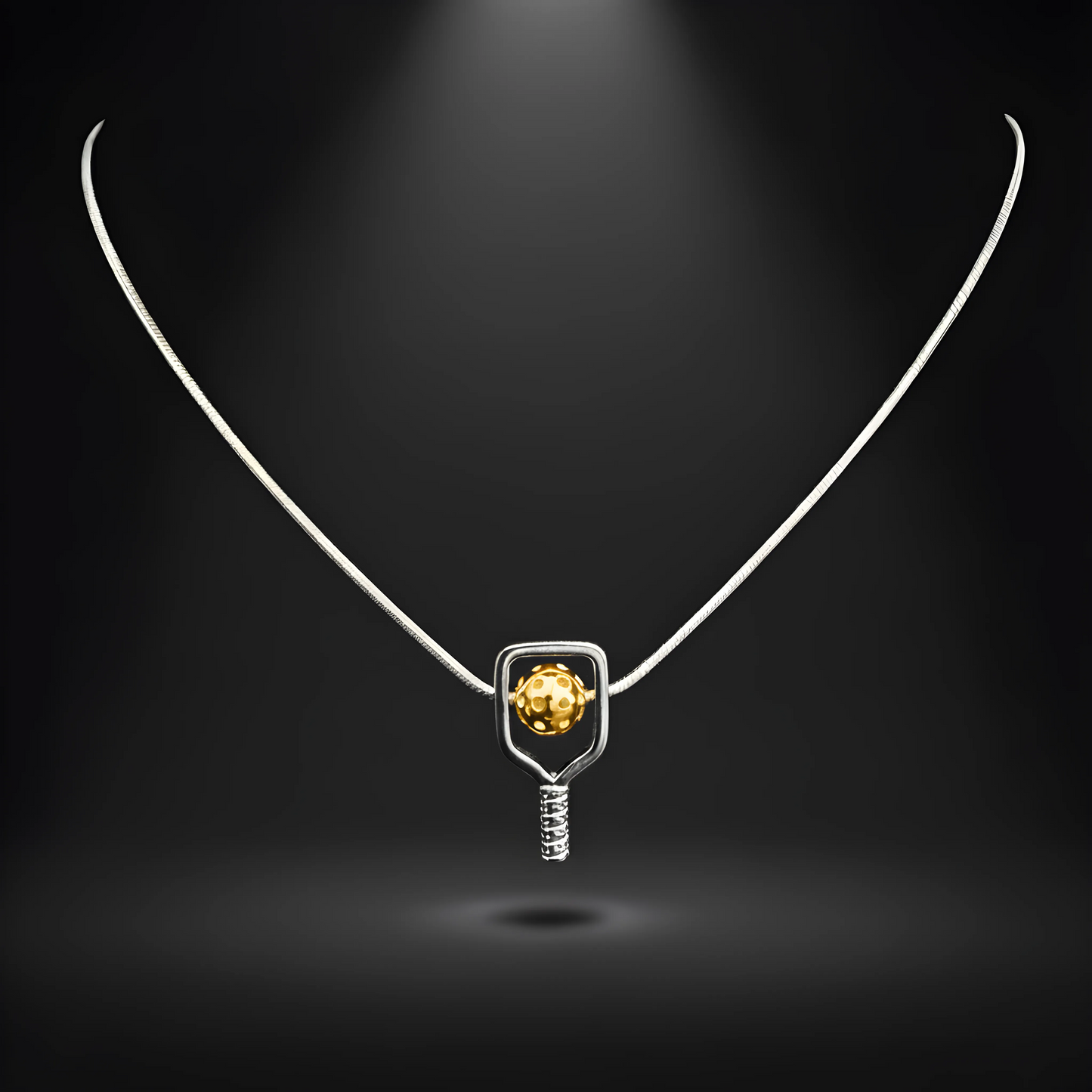 Necklace with a pendant featuring a silver paddle and a yellow pickleball on a dark background