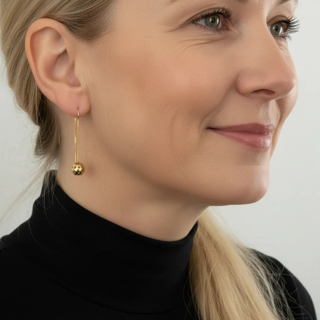 Close-up of a woman wearing gold earrings with pickleball dangle with a plain background