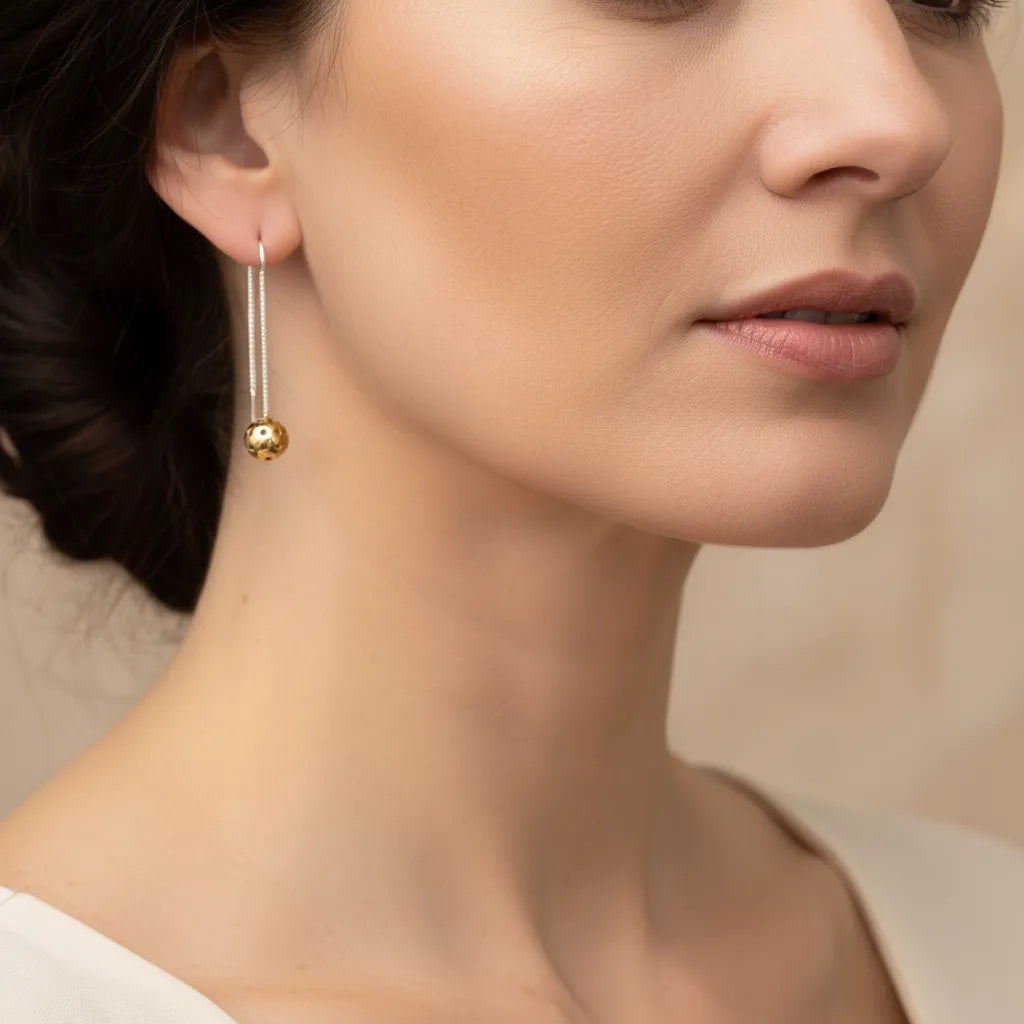 Close-up of a woman wearing silver earrings with a gold pickleball dangle with a neutral background.