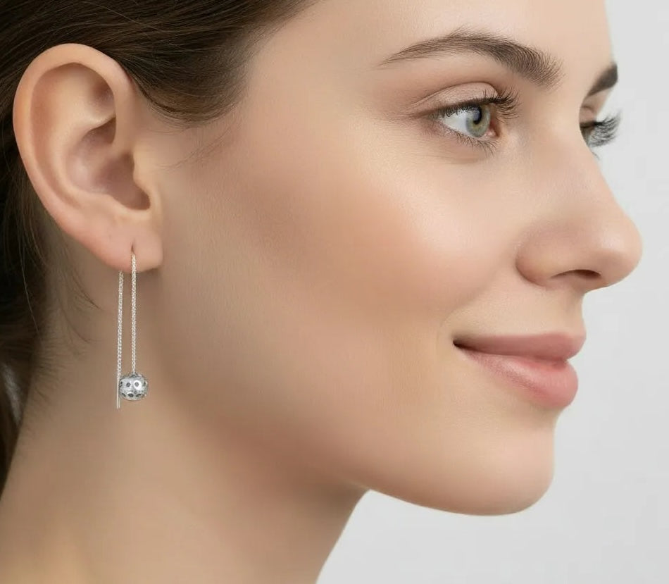Close-up of a woman wearing a silver earring with a pickleball dangle on a light gray background.
