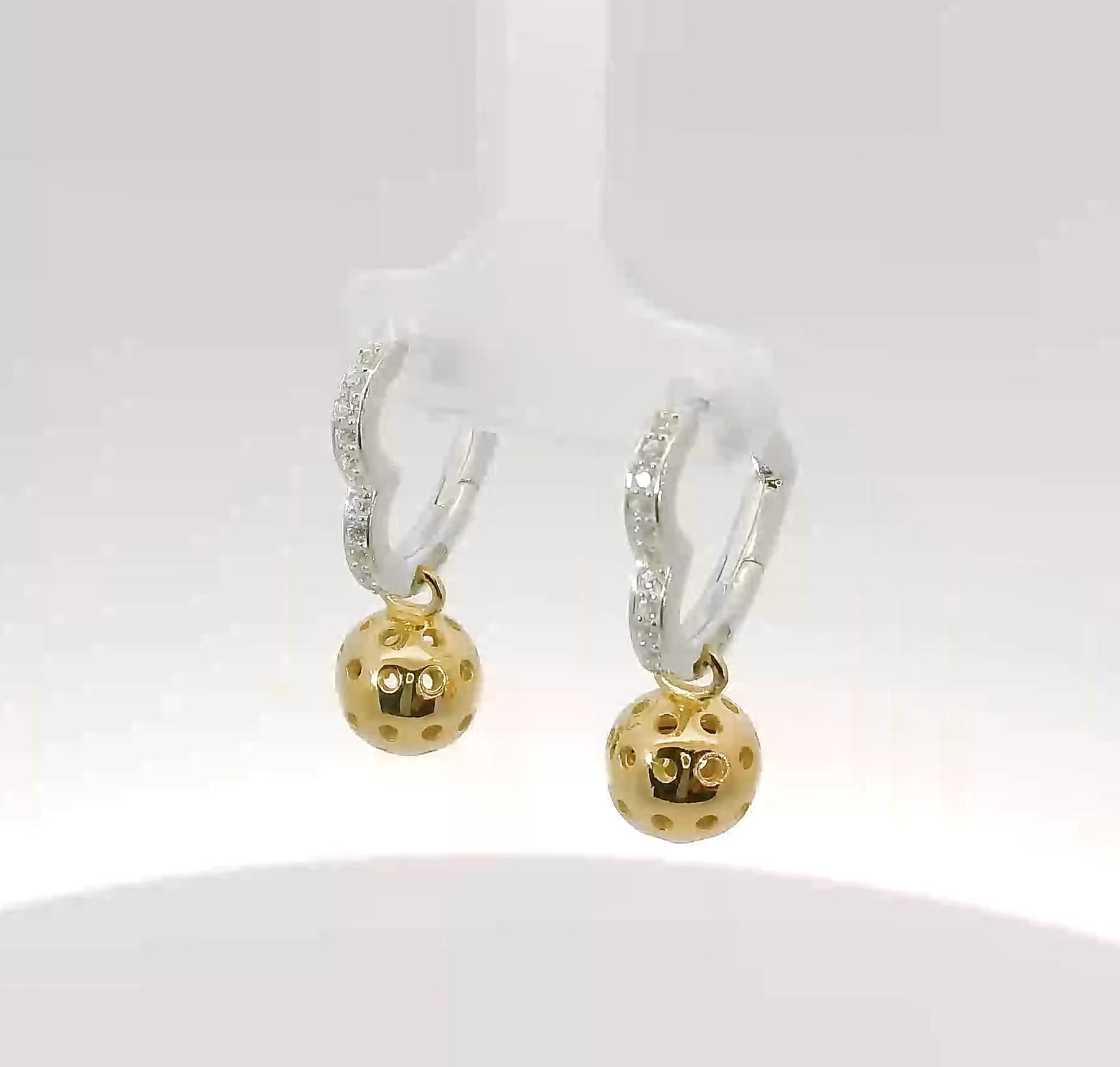Video of heart-shaped earring with white gemstones and gold dangle ball.